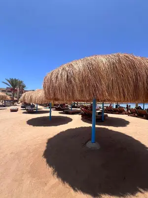 a beach with a straw umbrella and chairs on the sand at Hurghada Tiba Golden Resort Apartment Strand Pool 22 in Hurghada
