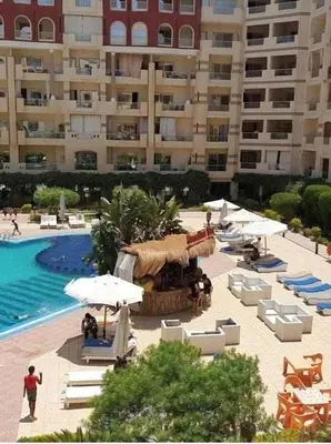 a pool with chairs and umbrellas next to a large building at Hurgada Florenza kamsen with pool view in Arabia area in Hurghada