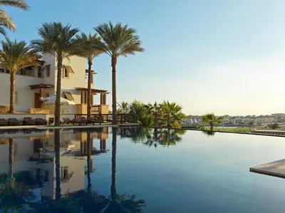 a swimming pool with palm trees and a building at Ancient Sands Golf Resort and Residences in Hurghada