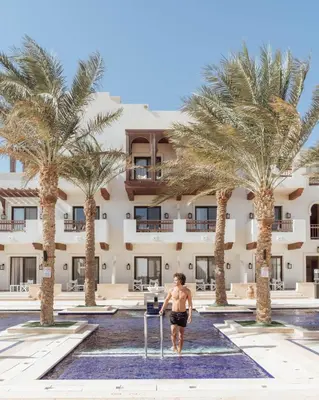 a man walking in front of a hotel with palm trees at Ancient Sands Golf Resort and Residences in Hurghada