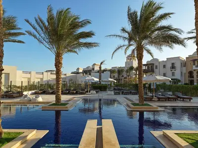 a pool with palm trees and buildings in the background at Ancient Sands Golf Resort and Residences in Hurghada