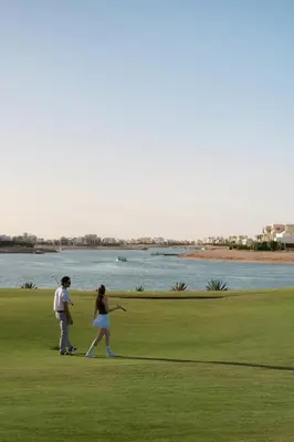 two people walking on a golf course near the water at Ancient Sands Golf Resort and Residences in Hurghada