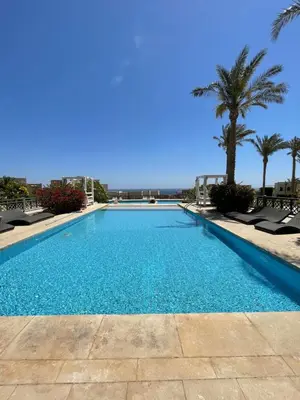 a swimming pool with chairs and palm trees at Cozy 1 bedroom Apartment in Azzurra Sahl Hasheesh in Hurghada