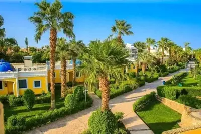 a yellow house with palm trees and a driveway at Mirage Bay Aqua Park Apartments in Hurghada