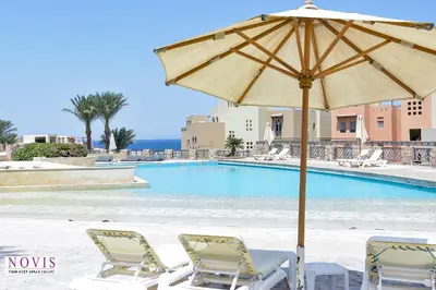 an umbrella and chairs next to a swimming pool at Novis Holiday Homes Sahl Hasheesh in Hurghada