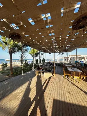 a covered deck with tables and benches and the beach at Luxury Apartment in Hurghada