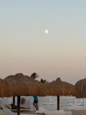 a person walking on a beach with some straw umbrellas at Luxury Newly Built 2 DOUBLE bedroom and living room with Beach Access and Pool in Hurghada, Egypt in Hurghada