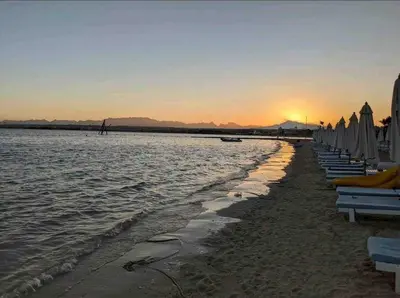 a beach with chairs and umbrellas at sunset at Luxurious Cozy studio in Sahl Hasheesh Hurghada in Hurghada