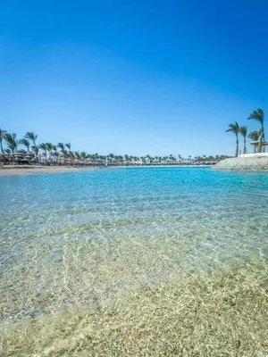 a beach with blue water and palm trees on it at ميراج باي اكوا بارك in Hurghada