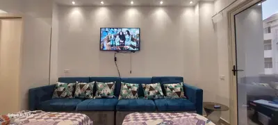 a living room with a blue couch and a tv on the wall at كمبوند فلورنزا خمسين عرابيا in Hurghada