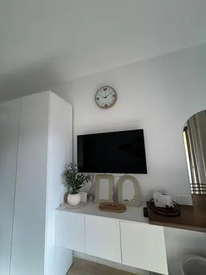 a flat screen tv on a white wall with a clock at Aldau Heights Modern Serenity Studio in Hurghada