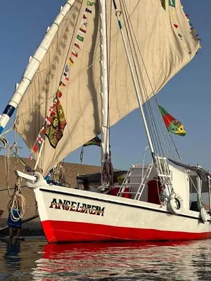a red and white sail boat in the water at Aswan felucca sailing boat in Aswān