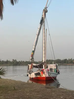 a boat with a crane sitting in the water at Aswan felucca sailing boat in Aswān