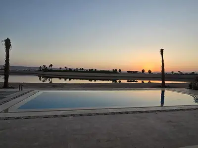 a pool of water with palm trees and a sunset at El Gouna Cyan Ringe Villa with infinity pool in Hurghada