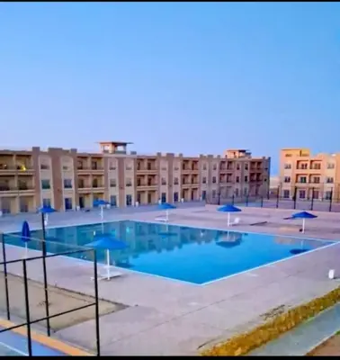 a large swimming pool with blue umbrellas and buildings at Bay View, Sahl Hashish in Hurghada