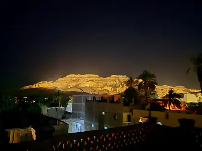 a view of a mountain at night with palm trees and buildings at FairHaven Apartments in Luxor