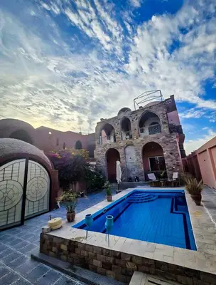 a villa with a swimming pool in front of a house at FairHaven Apartments in Luxor