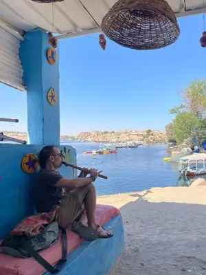 a man sitting on a boat playing a violin at Shamandora Nubian Guest House in Jazīrat Fīlah