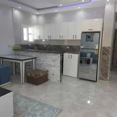 a kitchen with white cabinets and a table and a refrigerator at Veranda SH in Hurghada