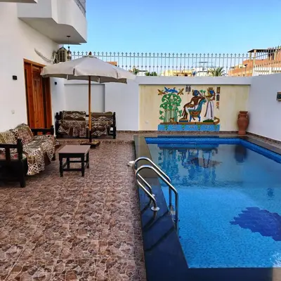 a large swimming pool with an umbrella and a table at Christine Home in Luxor