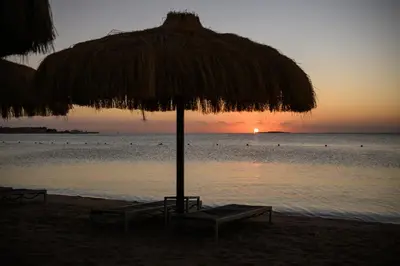 a straw umbrella and benches on the beach at sunset at Al Kasr Sahl Hasheesh - Ultra All-Inclusive in Hurghada