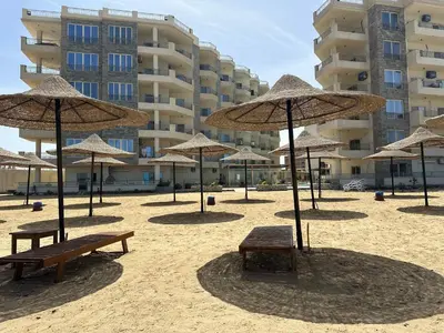 a beach with benches and umbrellas in front of a building at La-Quinta Resort Erika in Hurghada