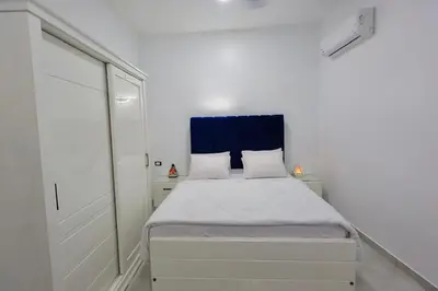 a white bedroom with a bed with a blue headboard at Al Mansi Luxury Retreat in Jazīrat al ‘Awwāmīyah