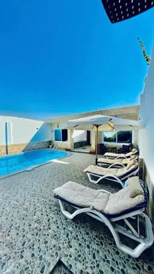a group of lounge chairs with an umbrella and a pool at Al Mansi Luxury Retreat in Jazīrat al ‘Awwāmīyah