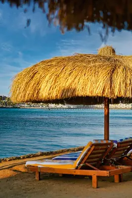 two lounge chairs under a straw umbrella on a beach at Tiba golden resort hurghada holiday in Hurghada