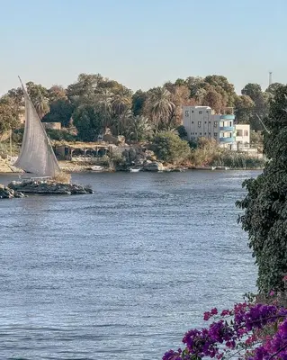 a sailboat on a river with a city in the background at Taha nubian boat in Jazīrat Aswān