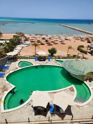 a large pool of green water next to a beach at Hurghada Seafront Family Apartment with Pool View in Hurghada