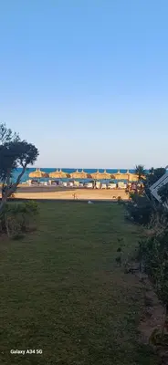 a field of grass with a beach with umbrellas at Luxury suit with private beach and aquapark in Hurghada
