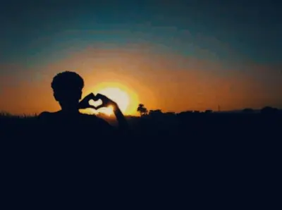 a man making a heart shape with the sunset in the background at High mountain in Luxor