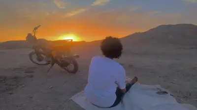 a person sitting next to a motorcycle in the desert at High mountain in Luxor