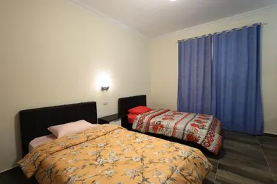 a bedroom with two beds and a window with blue curtains at Magawish Bliss , Elegant Hurghada Apartment in Hurghada