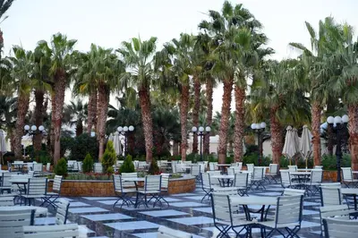 a patio with white tables and chairs and palm trees at Mirage Bay Resort Aquapark Ghada Suite in Hurghada