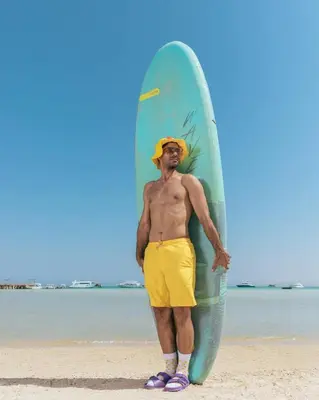 a man standing on the beach holding a surfboard at رحلات بحرية دولفين وغواصة وجزر in Hurghada