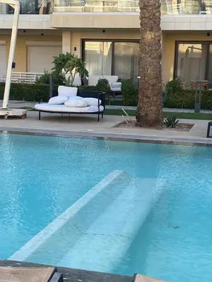 a blue swimming pool with a palm tree in front of a building at Chic G Cribs Studio in El Gouna