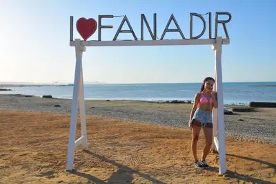 a woman standing under a sign on the beach at Fanadir Bay in Hurghada