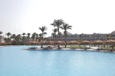 a large swimming pool with straw umbrellas and a resort at Xanadu Club Makadi Bay - High Class All Inclusive in Hurghada