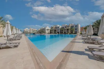 a large swimming pool with lounge chairs and umbrellas at Mangroovy - 2Br Commodious Pool&Gouna views Condo in Hurghada