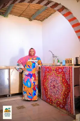 a woman standing in a kitchen next to a refrigerator at Heissa Nubian Hostel in Aswân Reservoir Colony