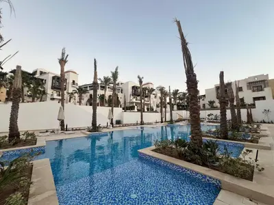 a swimming pool with palm trees and buildings at Stylish 1BR Retreat – Ancient Sands El Gouna in Hurghada