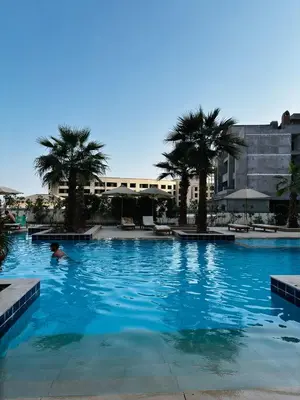 a person swimming in a large swimming pool with palm trees at Prime Square Aldau Heights in Hurghada