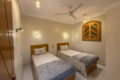 two beds in a room with a ceiling fan at Oscar Apartment 10 in Luxor