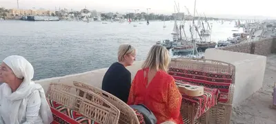 three women sitting on a ledge near the water at Nile Domes Guest House in Luxor