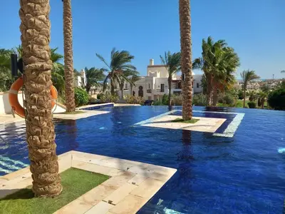a swimming pool with palm trees in front of a house at Scenic Cosy Nest - Infinity Pool - Ancient Sands in Hurghada