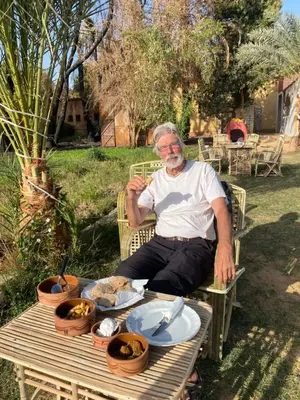 an older man sitting on a bench next to a table at Bafana Bafana Nile View Guest House in Aswan