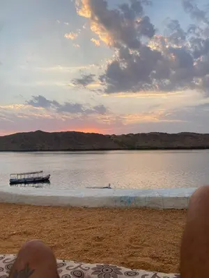 a person sitting on a beach with a boat in the water at Per Ankh - Heissa island - Aswan in Aswan