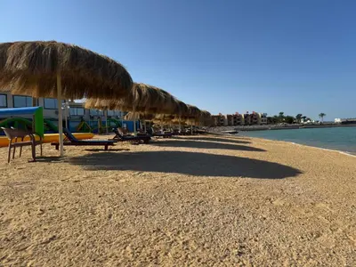 a beach with chairs and straw umbrellas and the water at Aquatic Village - Red Sea Resort in Hurghada